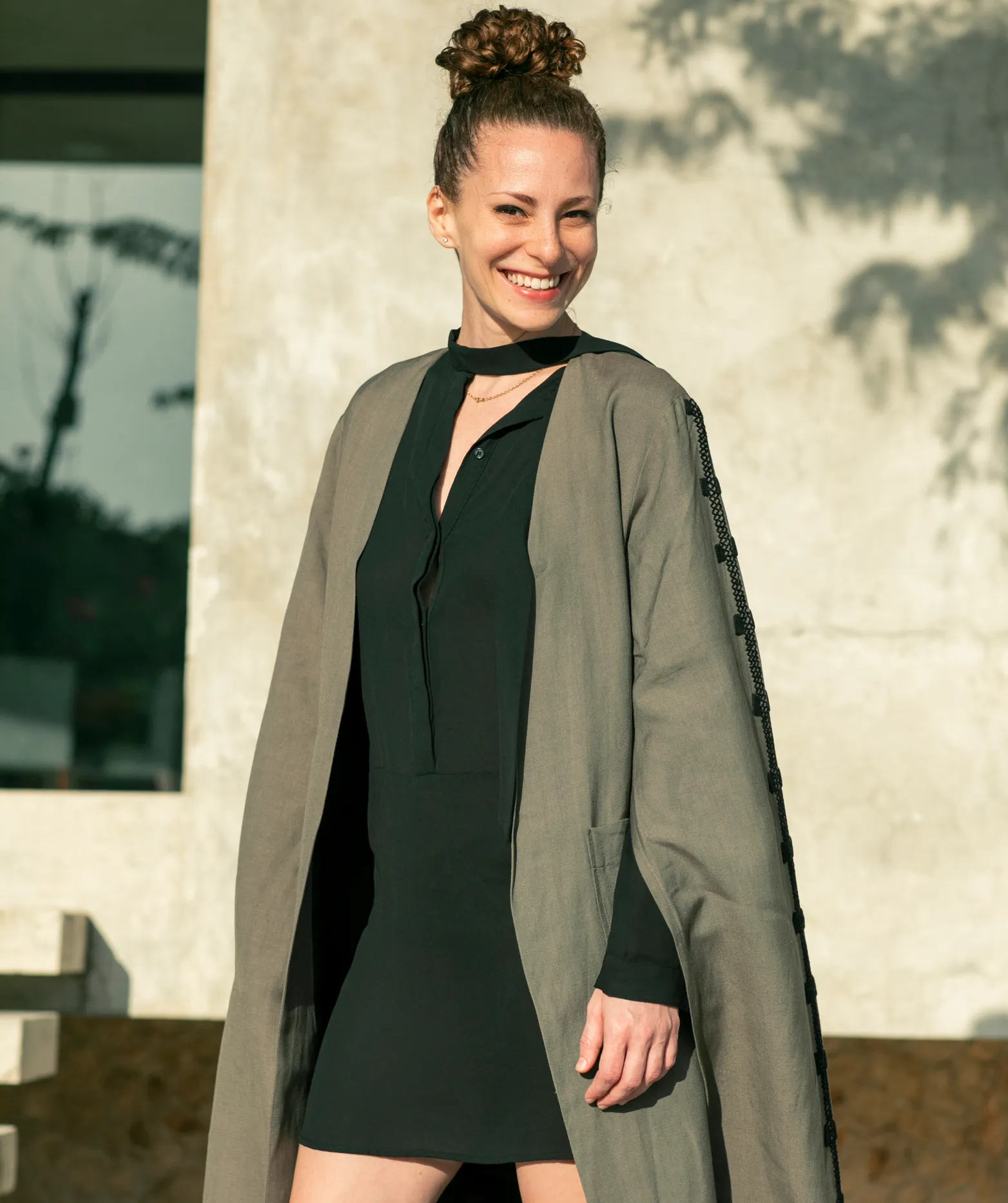 Krystal Ariel smiling confidently, dressed in a stylish black dress and gray coat, embodying her diverse experiences from yoga to digital marketing